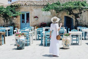 A woman in a white dress and hat walking past a building with a sign reading "Taverna La Ciuola".