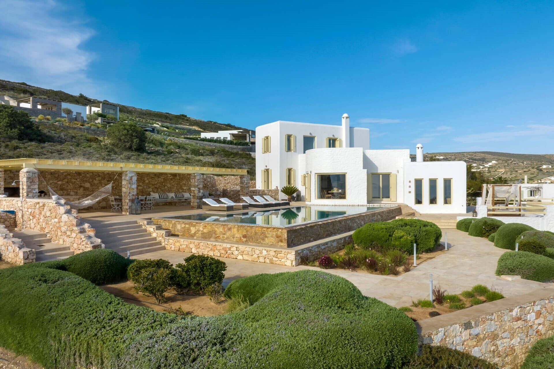 Eine moderne, weiße Villa mit Swimmingpool, Steintreppe und üppiger Bepflanzung.