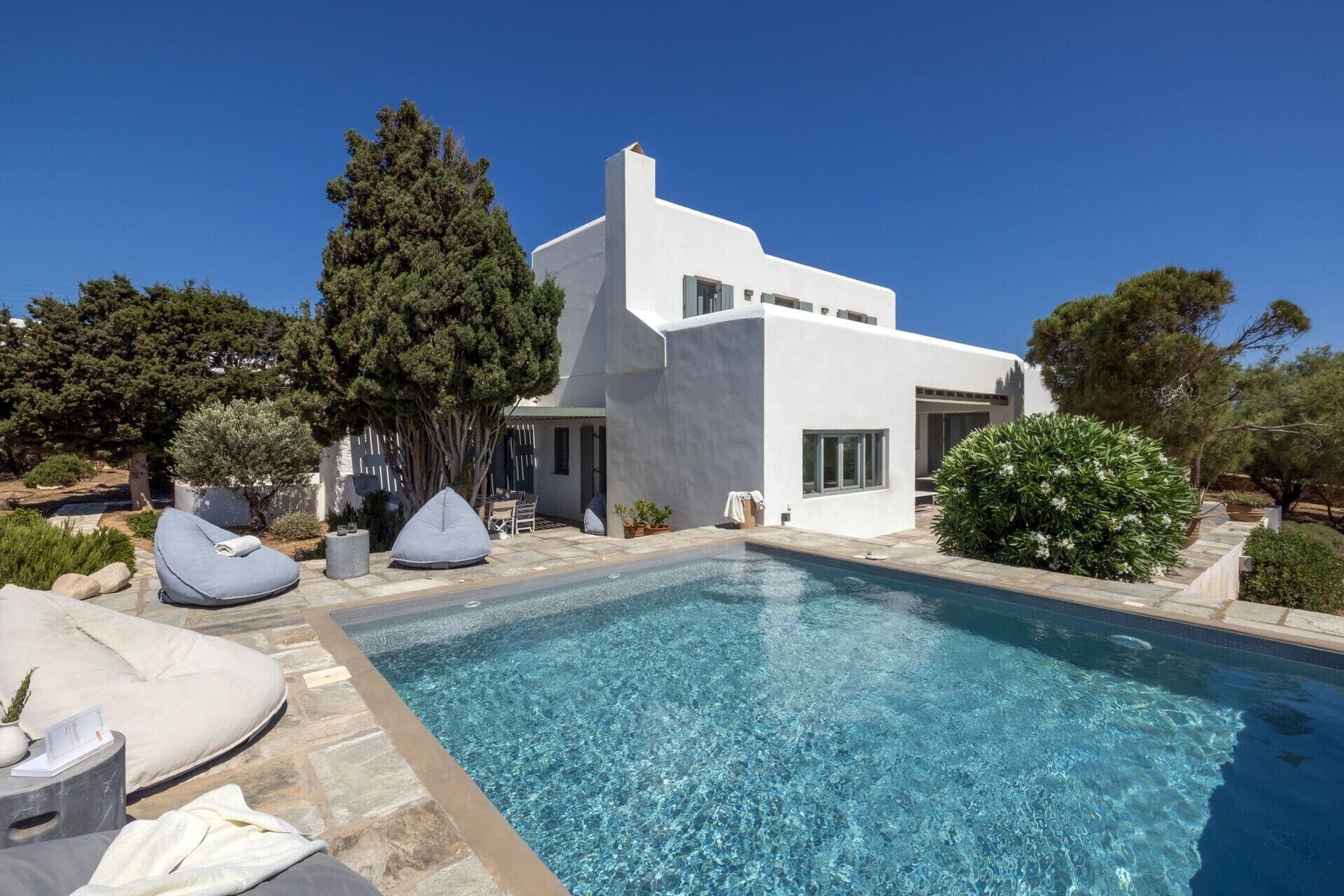 Et moderne hus med swimmingpool, udendørs møbler og en have.