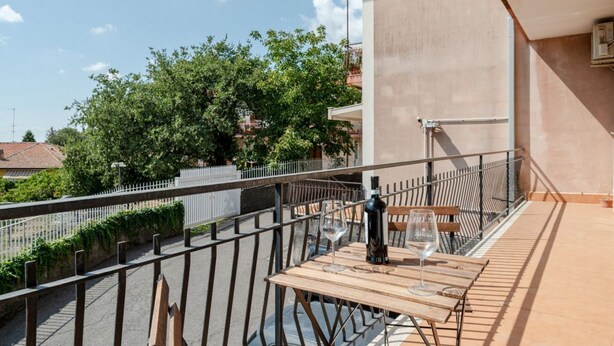 A balcony with a table, chairs, and a bottle of wine.