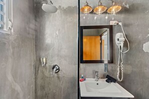 Une salle de bain avec un mur en béton, un lavabo blanc, un miroir, une douchette à main et un sèche-cheveux.