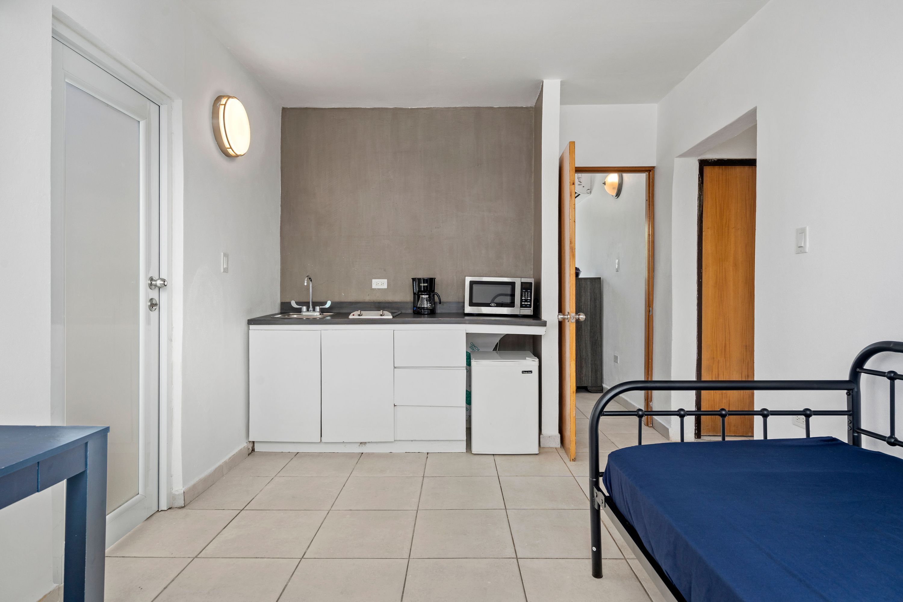A compact room with a bed, a kitchenette, and a small fridge.