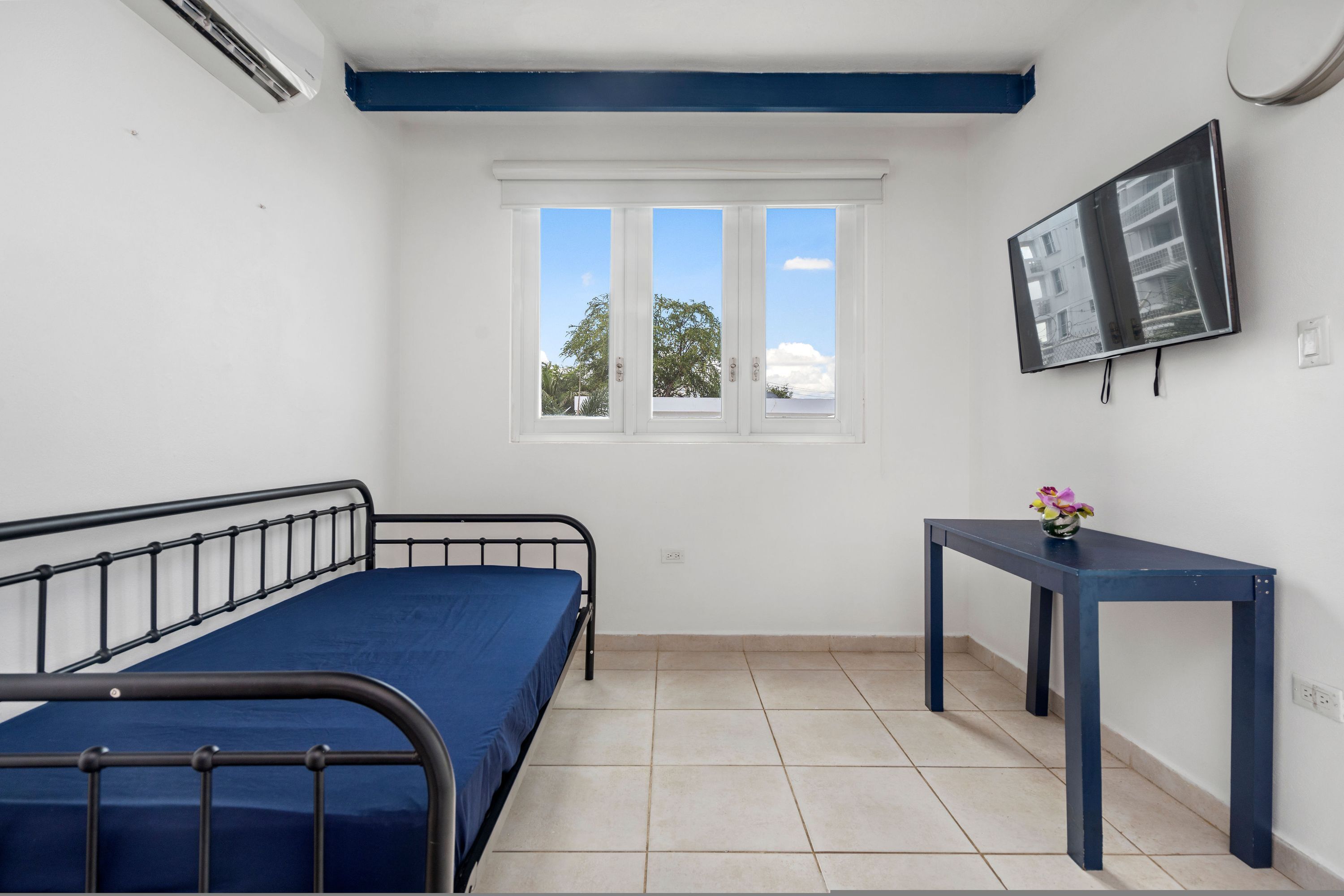 A small, clean room with a bed, a table, and a TV.