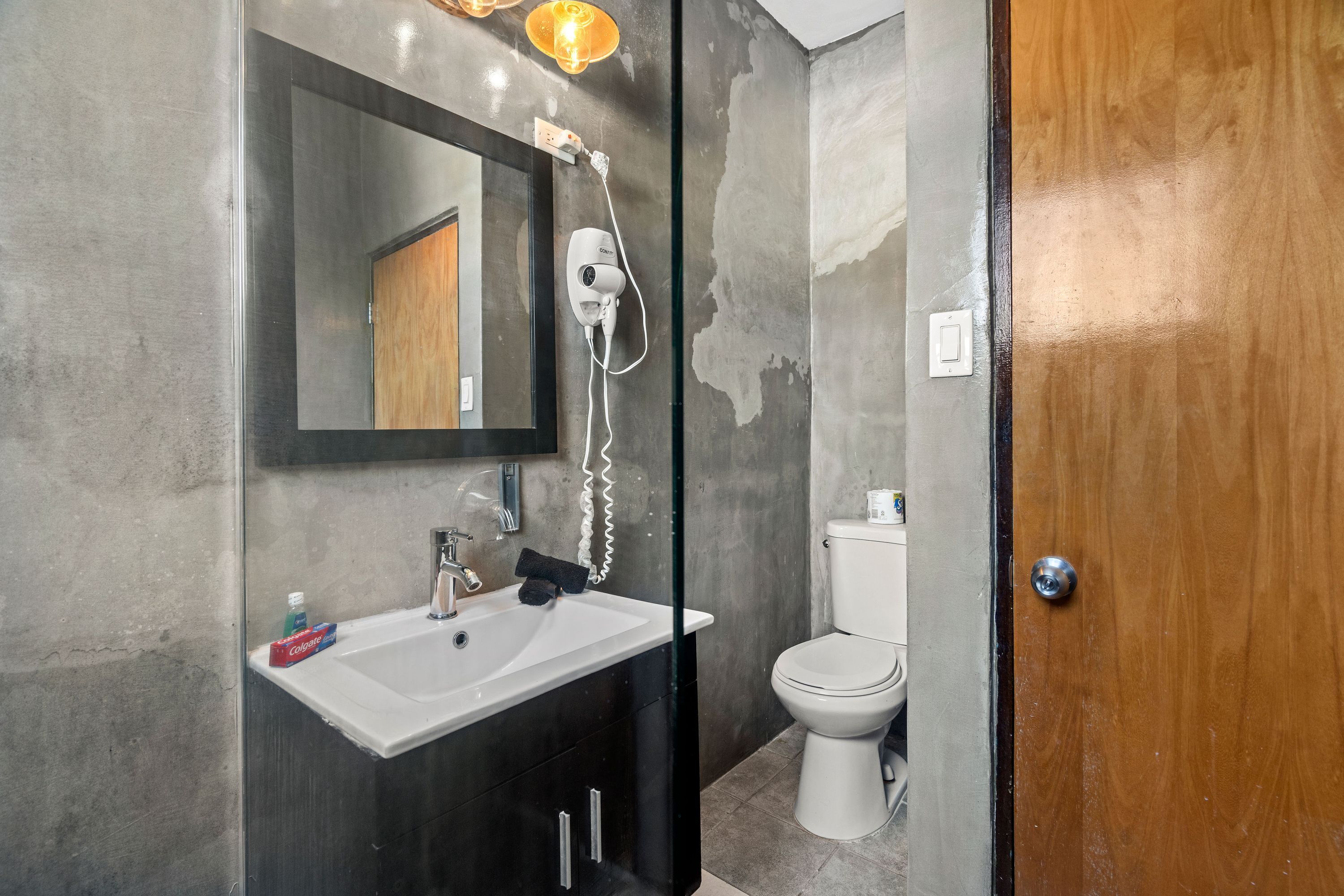 Uma casa de banho moderna com uma pia branca, um espelho, um secador de cabelo e uma sanita.