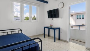 Una habitación con una cama, una mesa con un florero, un televisor y una ventana con vistas a edificios.