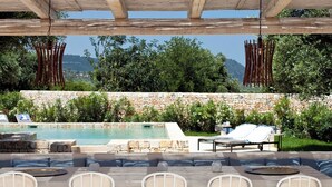 Zona de piscina exterior con muros de piedra, sillones de descanso y una pérgola.
