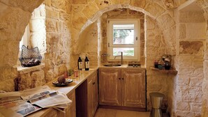 Cocina con paredes de piedra, ventana, pileta y armarios de madera.