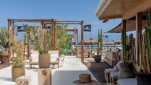 Un área de estar al aire libre con mobiliario de madera, plantas en macetas y una pérgola de bambú.