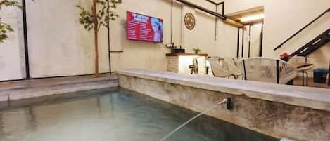 A swimming pool with a stone edge, a reception desk, and a mounted television.