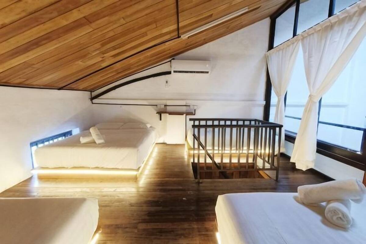A room with a sloped ceiling, a crib, a bed, and a window with curtains.
