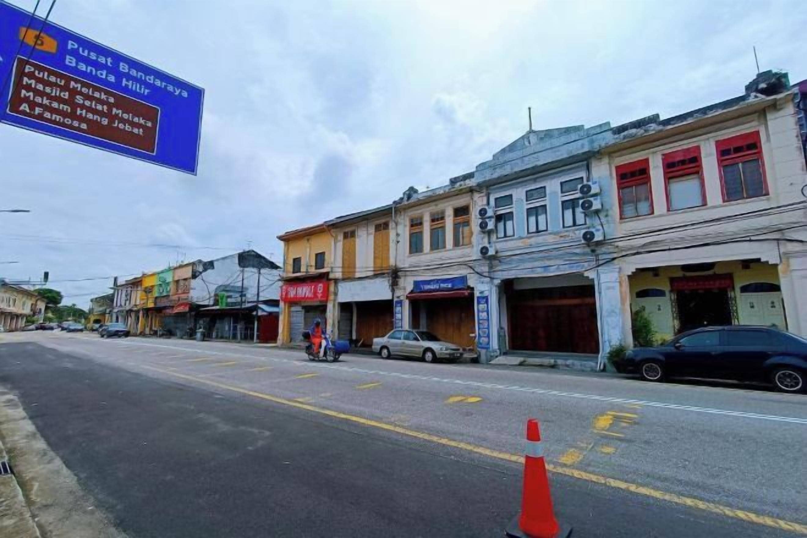 A street view with commercial buildings, a signboard, and a few vehicles.