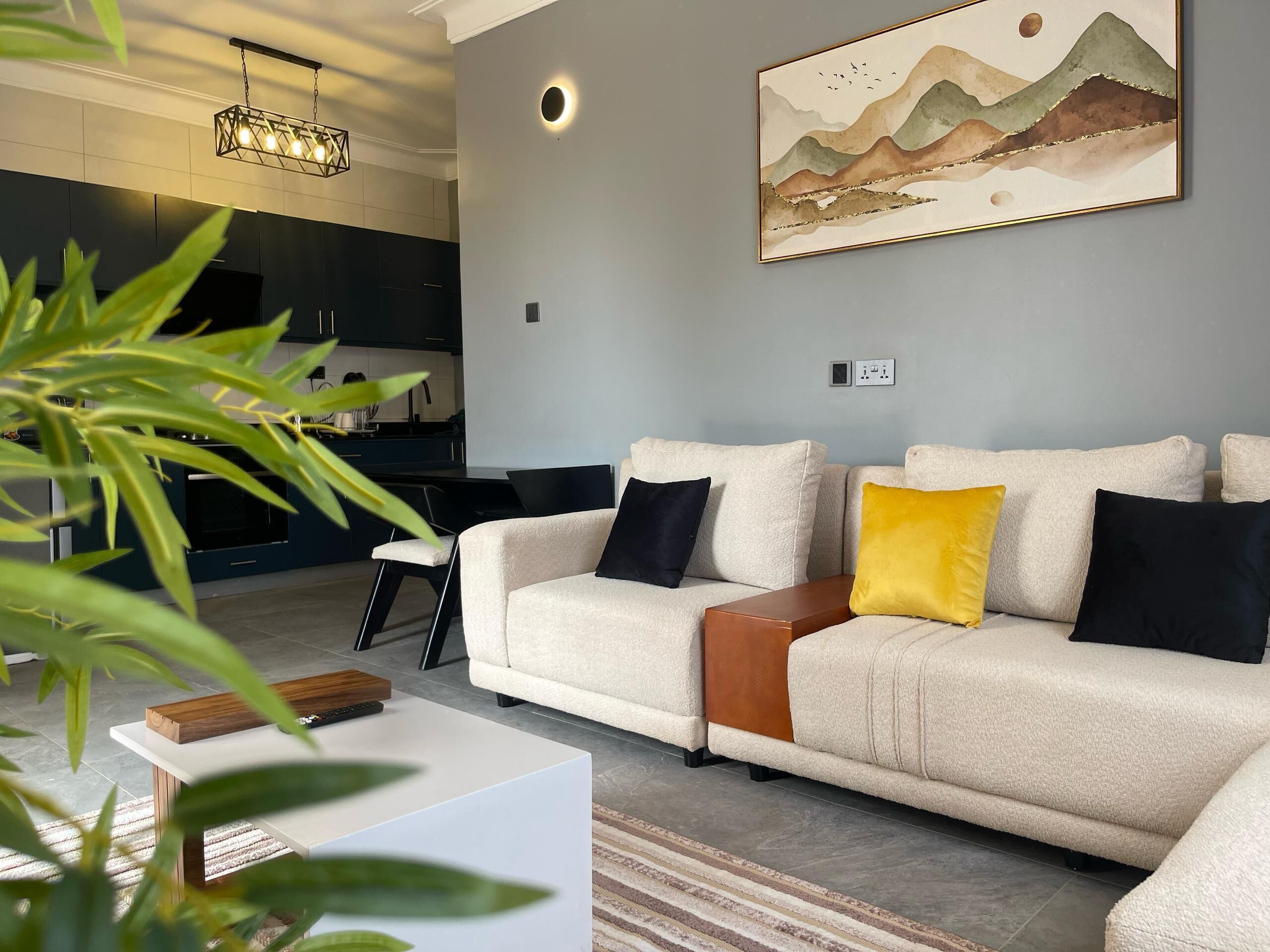 A modern living room with a beige sofa, a coffee table, and a painting of mountains on the wall.