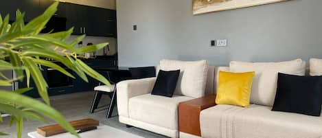 A modern living room with a beige sofa, a coffee table, and a painting of mountains on the wall.