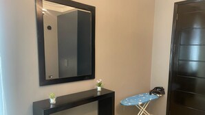 Une salle de bain avec un meuble-lavabo noir, un miroir, une petite plante en pot et une planche à repasser recouverte d’un tissu bleu.