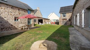 Un bâtiment en pierre avec une cour verdoyante, des sièges en plein air et un espace abrité.