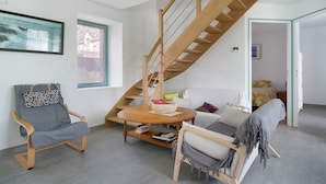 Un intérieur moderne avec un escalier en bois, une table ronde en bois et un fauteuil gris.
