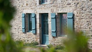 Un bâtiment en pierre avec une porte et des volets bleus, un petit porche et un jardin.