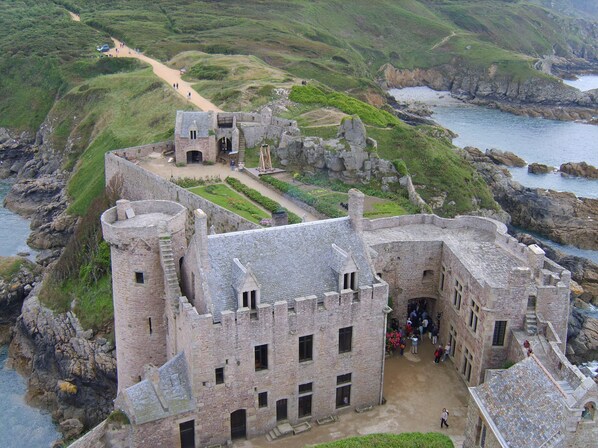 A historic stone castle with a central courtyard, surrounded by rocky cliffs and a coastal view.