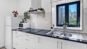 Een moderne keuken met een zwart aanrecht, witte kasten, een ingebouwde magnetron en een raam met uitzicht op groen.