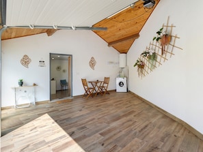 A room with a wooden ceiling, a washing machine, a dining table with chairs, and a small table with a plant.