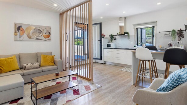 Een moderne woonkamer met een bank, salontafel en een eethoek met krukken.
