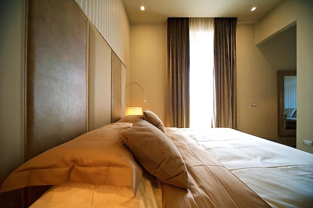 A hotel room with a large bed, a bedside lamp, and a view of the outside through a window with curtains.