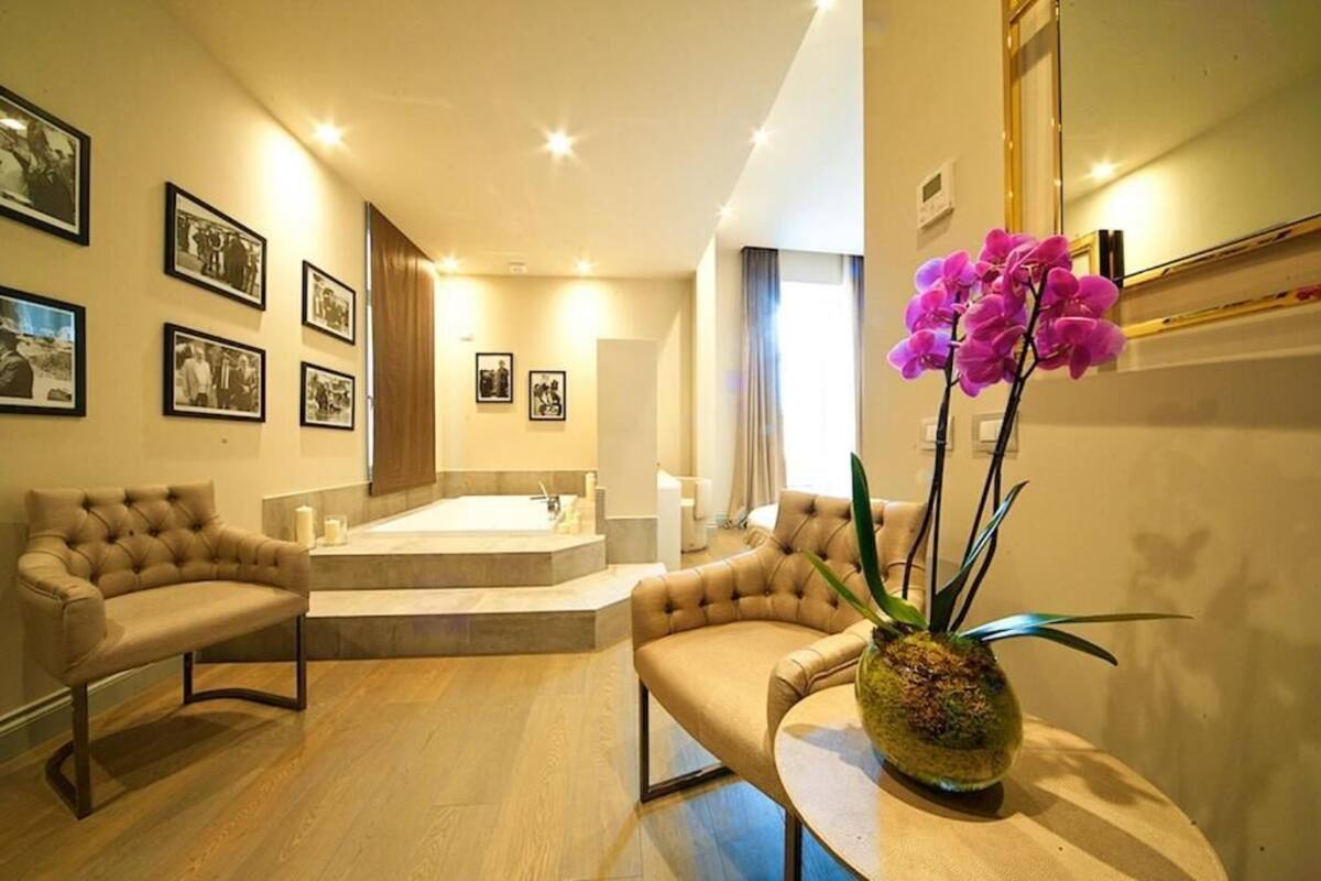 A modern bathroom with a bathtub, a toilet, and a sink. There are two chairs and a table with a vase of flowers.