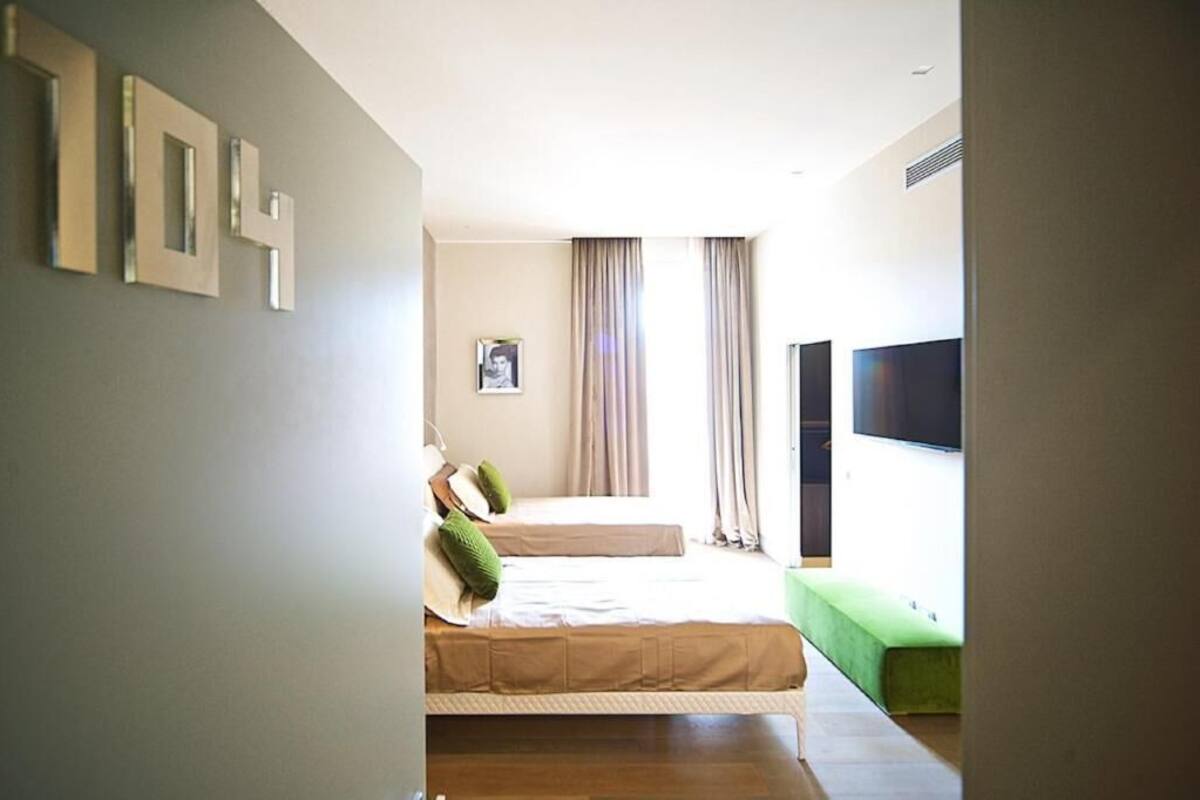 A modern hotel room with a large bed, a flat-screen TV, and a green bench.