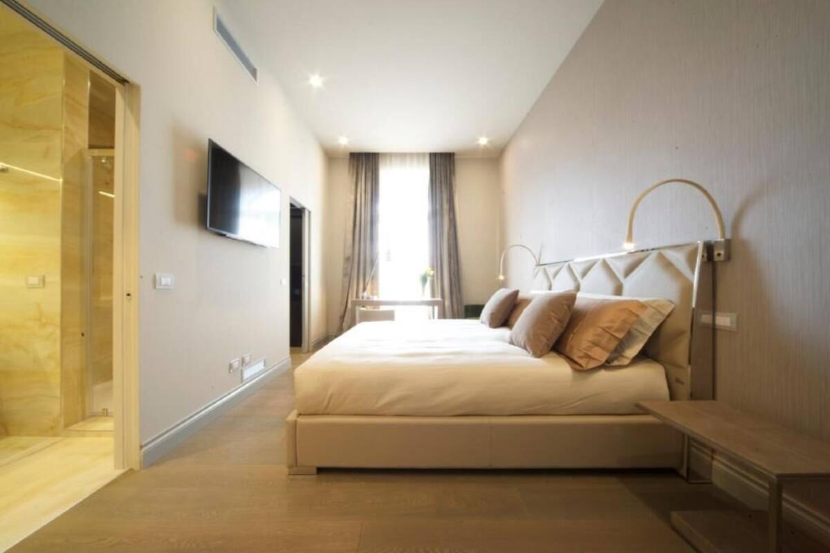 A bedroom with a bed, a TV mounted on the wall, and a window with curtains.