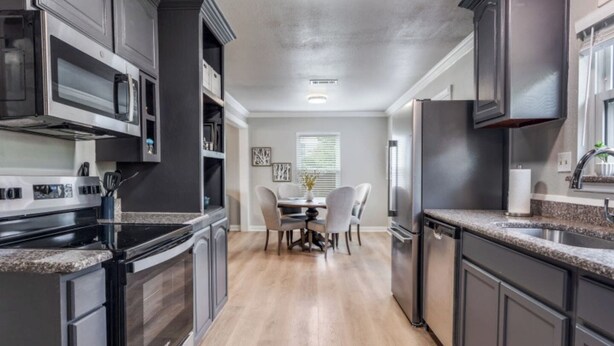 A modern kitchen with dark cabinetry, stainless steel appliances, and a dining area with a table and chairs.