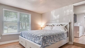 A bedroom with a bed, a nightstand, a lamp, a window with blinds, and a wardrobe.