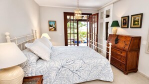 Un dormitorio con cama, cómoda, lámpara y vistas al exterior.