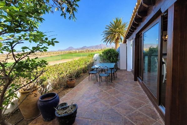 Une terrasse avec une table et des chaises, des plantes en pot et une vue sur un terrain de golf et des montagnes.