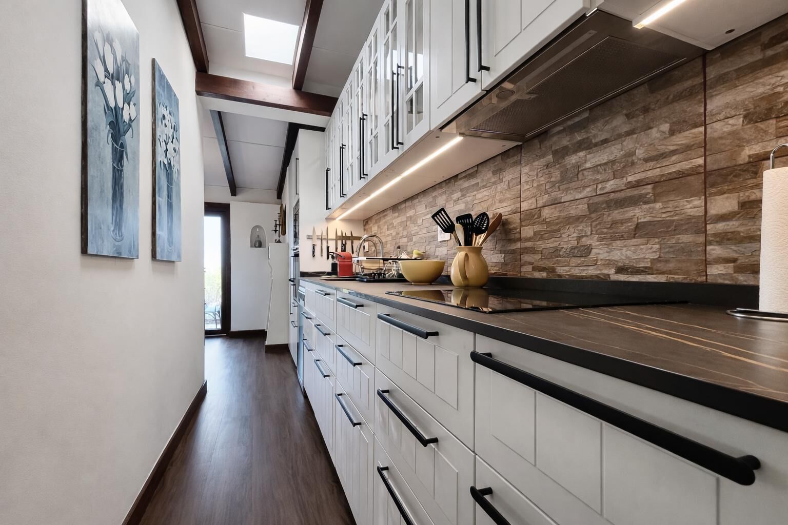 A modern kitchen with white cabinets, a stone backsplash, and a long countertop.