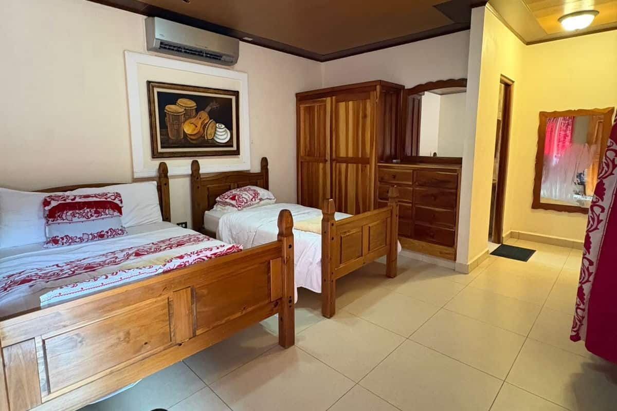 Un dormitorio con cama de madera, un banco, un armario y un cuadro en la pared.