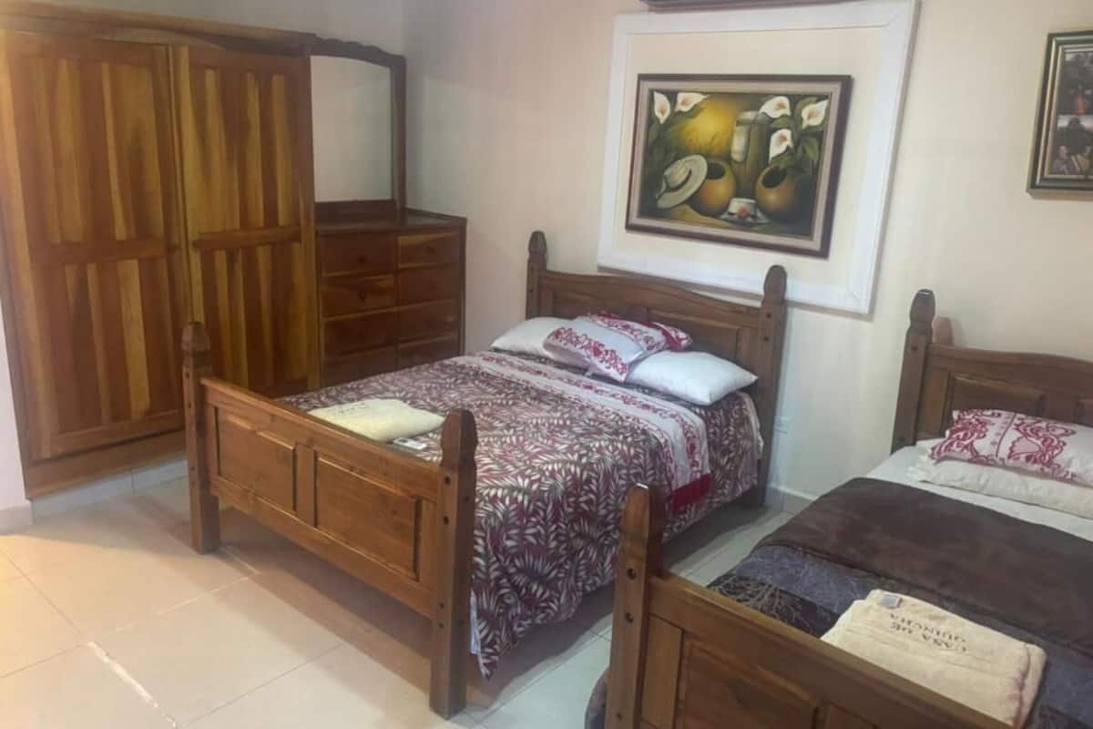 Un dormitorio con dos camas de madera, un armario de madera y un cuadro enmarcado en la pared.