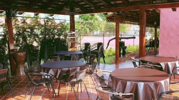 Patio esterno con tavoli e sedie rotonde, circondato da una pergola in legno e un pavimento in mattoni.