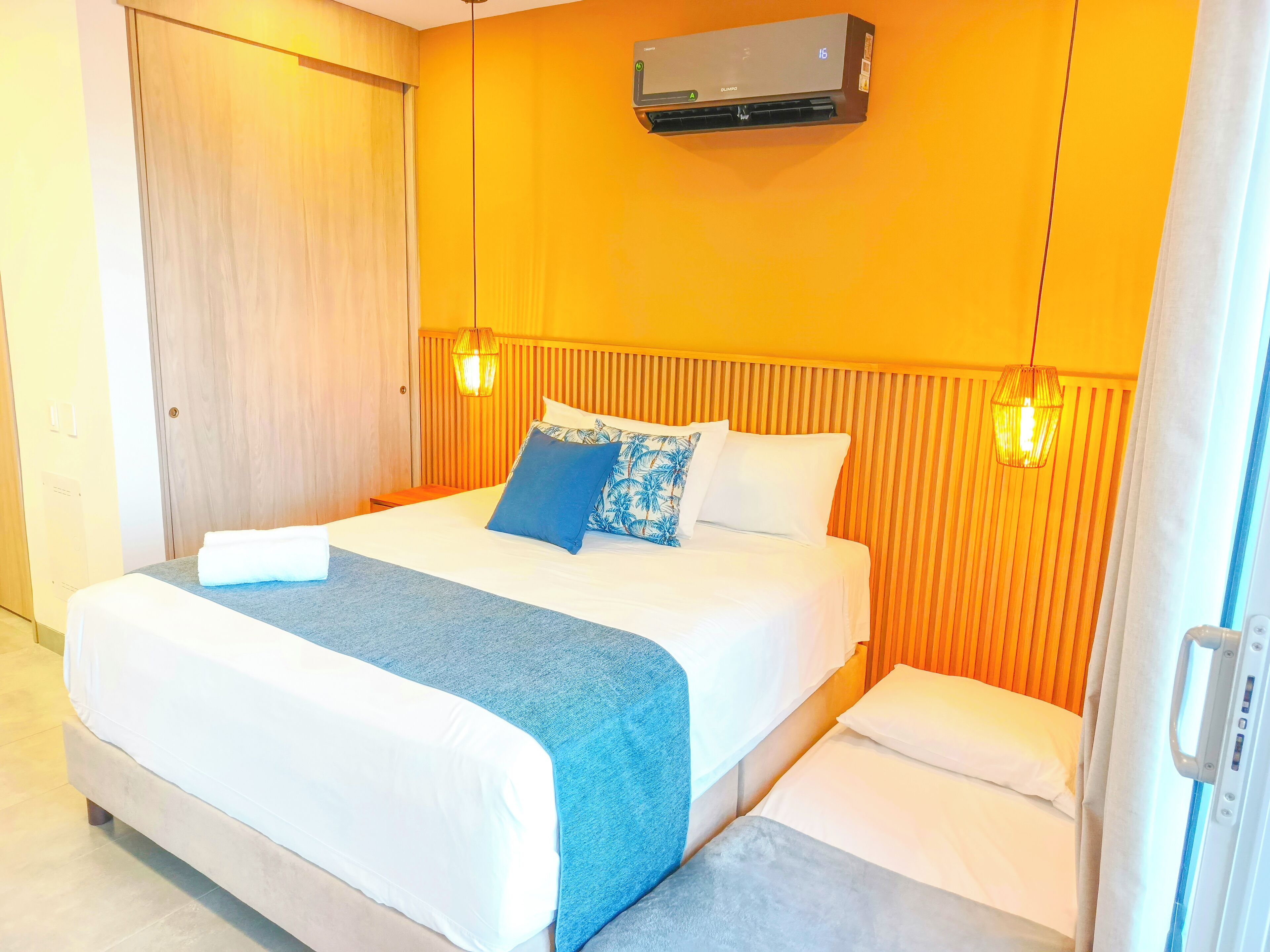 Habitación de hotel con cama, mesitas de noche, aire acondicionado y ventana con cortinas.
