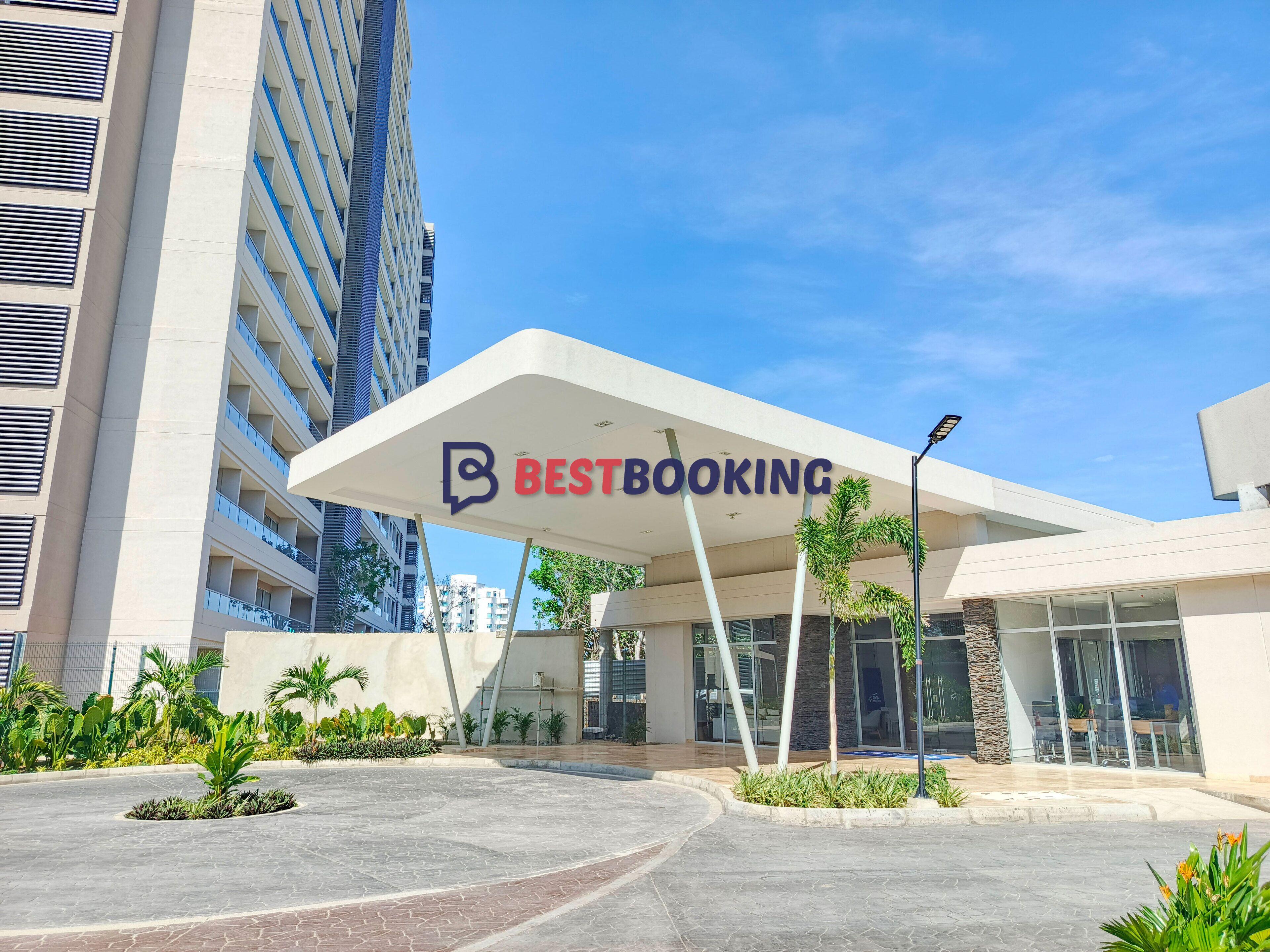 Een modern gebouw met een 'BestBooking' bord, omringd door groen en andere gebouwen.
