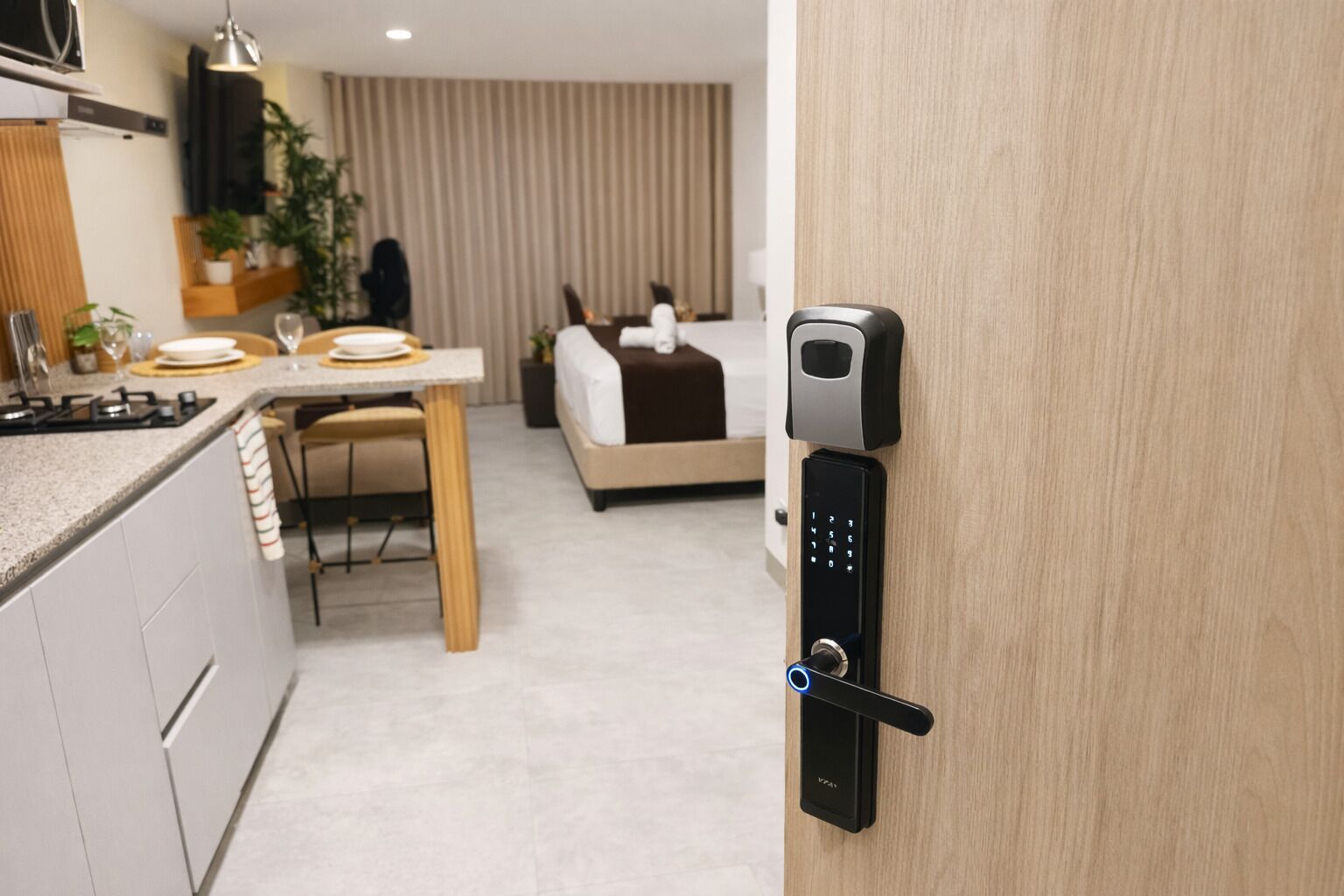 A modern hotel room with a kitchen area, a dining table, and a bed.