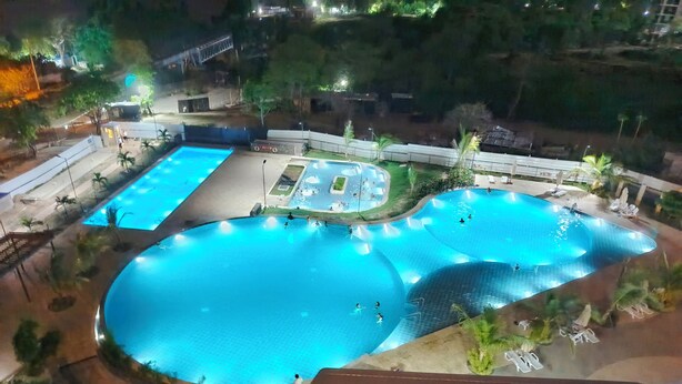 Una gran piscina al aire libre con varias secciones, rodeada de palmeras y una zona bien iluminada.