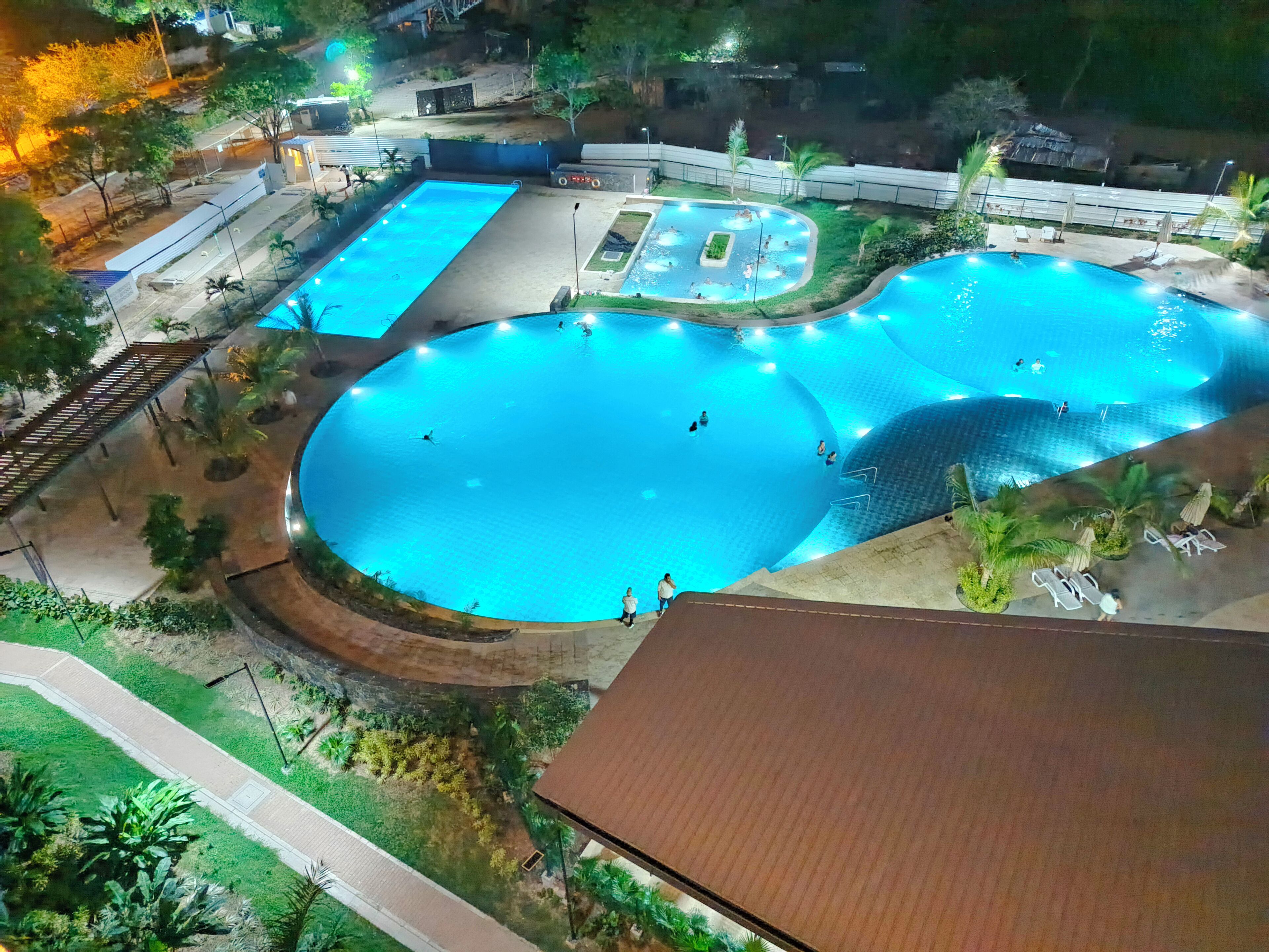 Un grand complexe de piscines illuminées, comprenant plusieurs bassins et entouré de verdure.