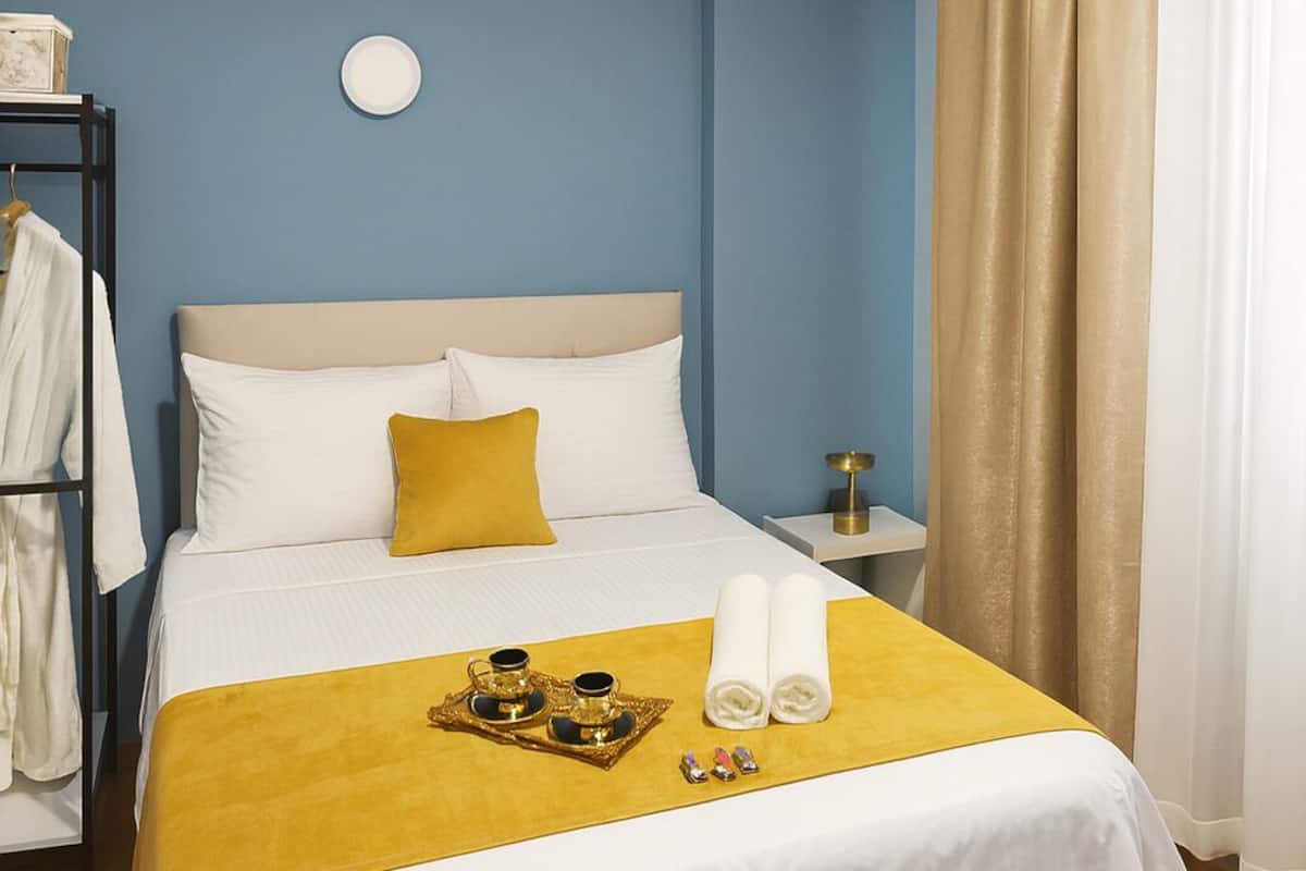A hotel room with a bed, a bedside table, a nightstand, a wardrobe, and a window with curtains.