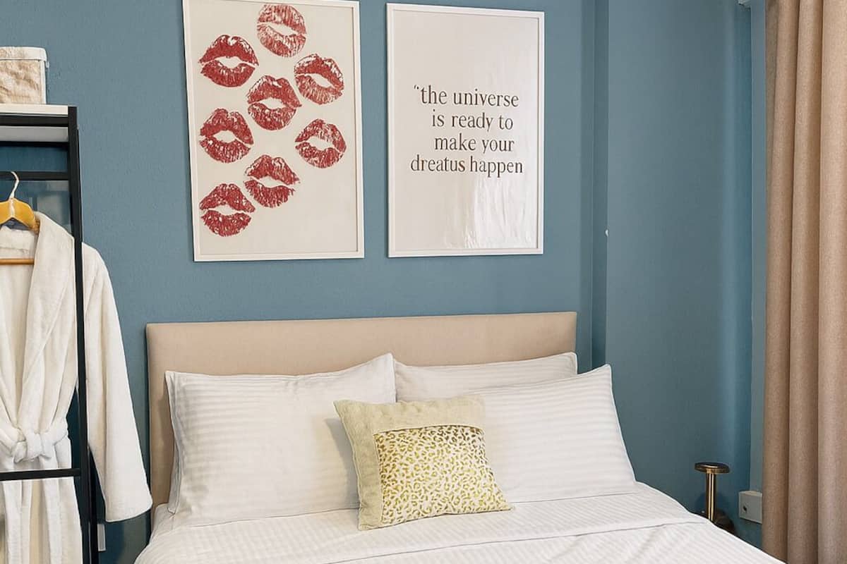 A neatly made bed with white linens, a mustard-colored throw blanket, and two folded towels on the bedside table.