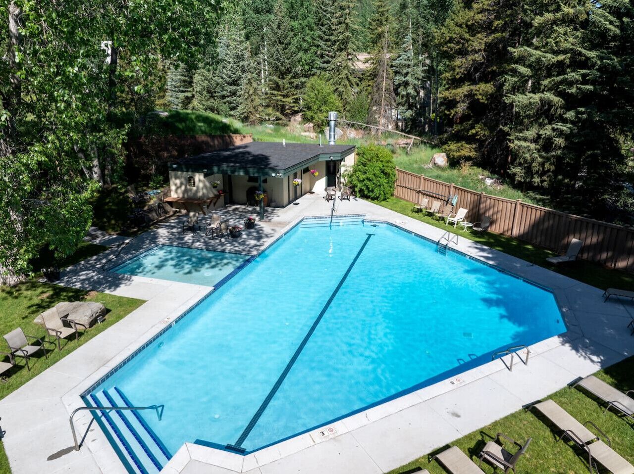 Una piscina rectangular con agua cristalina azul, rodeada por una cubierta de madera y un césped.