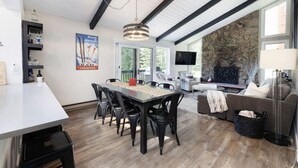 Un vaste espace de vie agrémenté d’une cheminée en pierre, d’une table à manger avec des chaises, d’un canapé et d’un téléviseur fixé au mur.