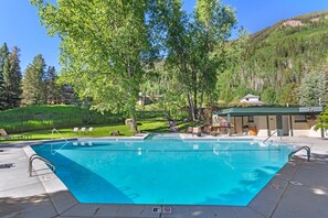 Uma piscina azul cristalina com um deck, espreguiçadeiras e um pequeno edifício com telhado.