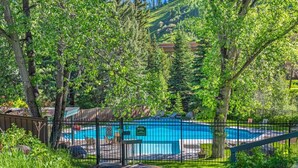 Une piscine entourée d’une clôture, avec des arbres et une colline en arrière-plan.