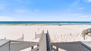 Een strand met een houten looppad dat naar het water leidt, zandstrand en een helderblauwe lucht.