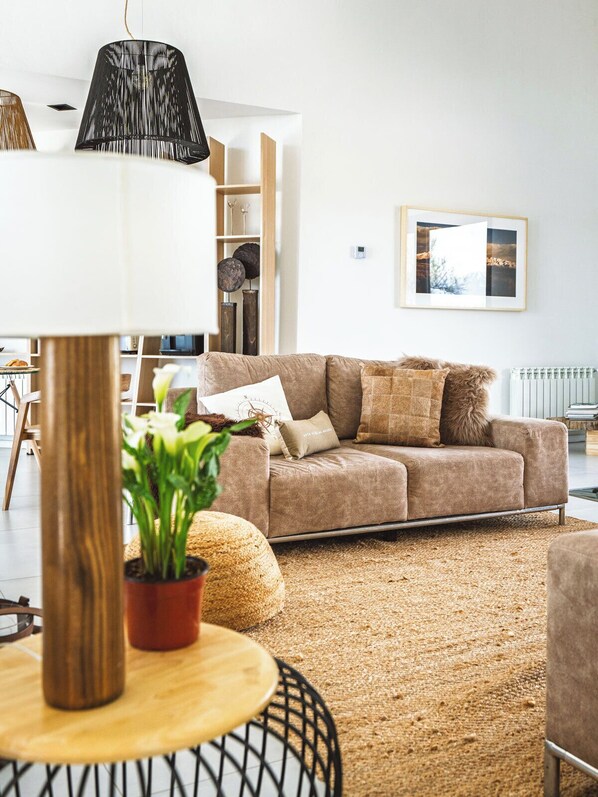 A modern living room with a sofa, a round wooden table with a potted plant, a black lamp, and a framed picture on the wall. - Terra Uco Suites & Viñedos (Vista Flores)